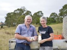 An pair of dairy farmers holding milk and cheese on the back of a ute with trees in the background. They are representative of some of the farmers and producers using the open food network to hold a virtual farmers market.  